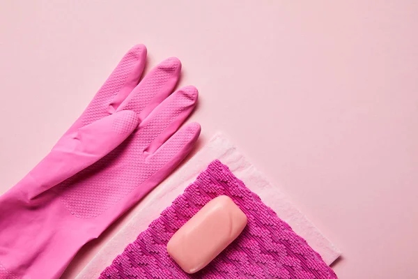 Vista superior de trapos rosados, guante de goma y jabón sobre fondo rosa - foto de stock