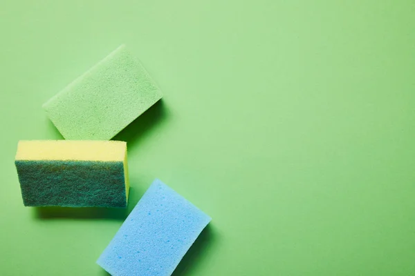 Vue de dessus des éponges jaunes, bleues et vertes sur fond vert — Photo de stock