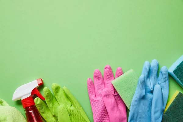 Top view of colorful rag, rubber gloves, spray and sponges on green background — Stock Photo