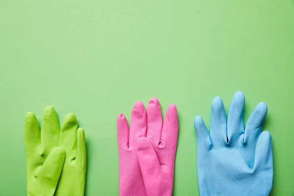 Вид зверху яскравих і барвистих гумових рукавичок на зеленому фоні — стокове фото