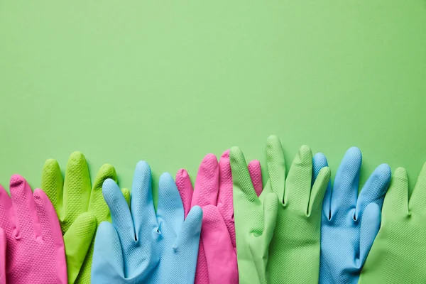 Вид зверху барвисті і яскраві гумові рукавички на зеленому фоні — стокове фото