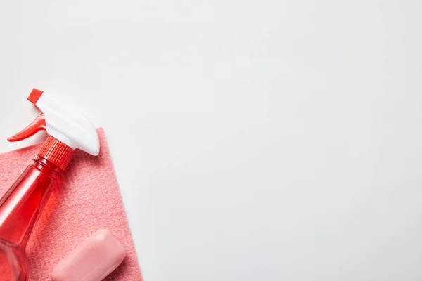 Vista superior de trapo rosa, jabón y botella con spray sobre fondo gris - foto de stock