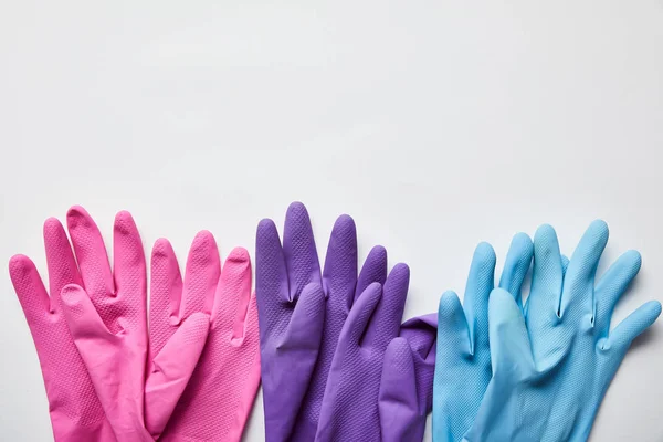 Вид сверху розовых, фиолетовых и синих резиновых перчаток на сером фоне — стоковое фото