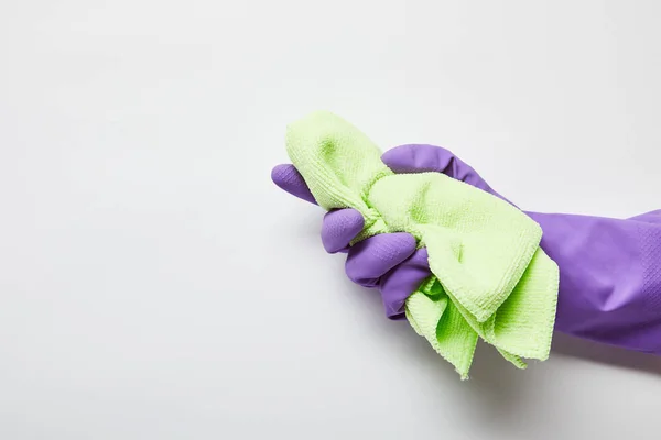 Обрезанный вид человека в фиолетовой резиновой перчатке с зеленой тряпкой — стоковое фото