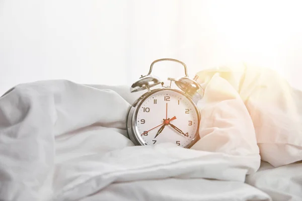 Silver alarm clock on blanket in white bed with sunlight on background — Stock Photo