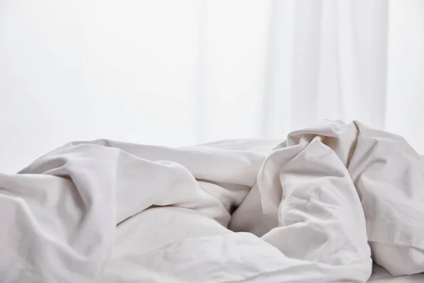 Смятое белое одеяло в постели рядом с занавесом — стоковое фото