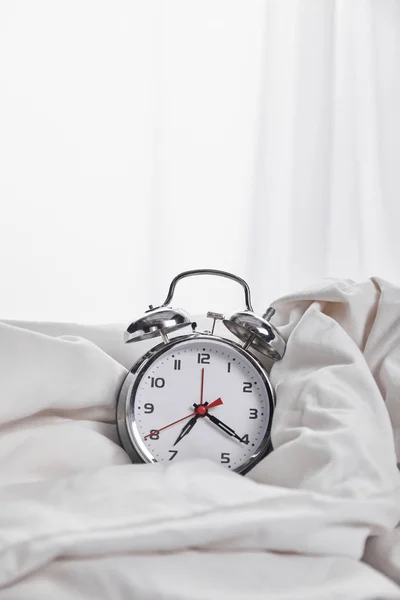 Silver alarm clock in blanket in white bed — Stock Photo