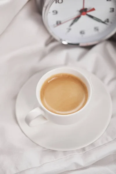 Vue du dessus du café en tasse blanche sur la soucoupe près du réveil en argent sur la literie — Photo de stock