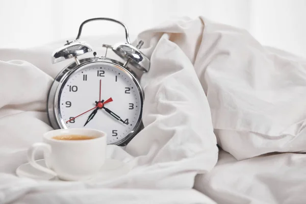 Café na xícara branca no pires perto de relógio de alarme de prata em cobertor branco — Fotografia de Stock