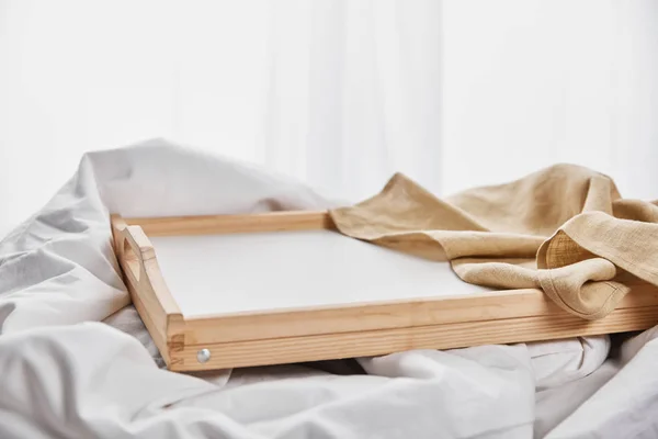 Guardanapo bege na bandeja de madeira na cama branca — Fotografia de Stock
