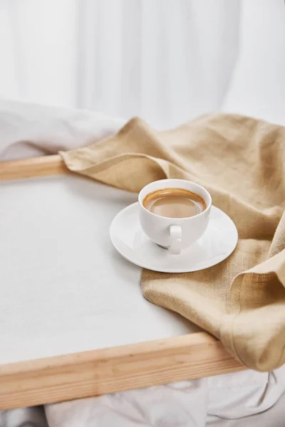Café en tasse blanche sur soucoupe près de serviette beige sur plateau en bois — Photo de stock