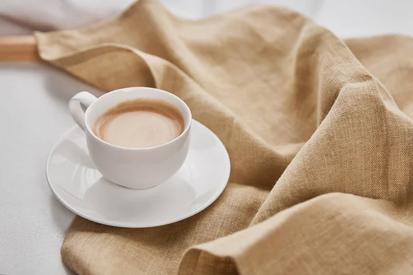 Close up view of coffee in white cup on saucer near beige napkin — Stock Photo