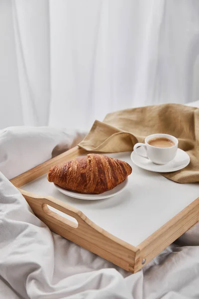 Fresh croissant with coffee on wooden tray with beige napkin — Stock Photo