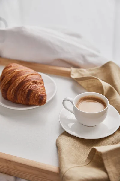 Croissant fresco su piatto con caffè in tazza su vassoio di legno a letto al mattino — Foto stock