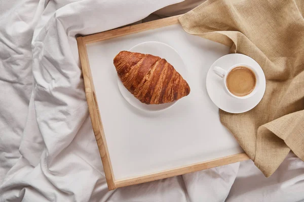 Draufsicht auf frisches Croissant mit Kaffee auf Holztablett im Bett am Morgen — Stockfoto