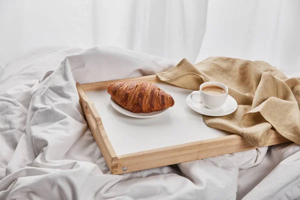 Fresh croissant with coffee and napkin on wooden tray in bed at morning — Stock Photo