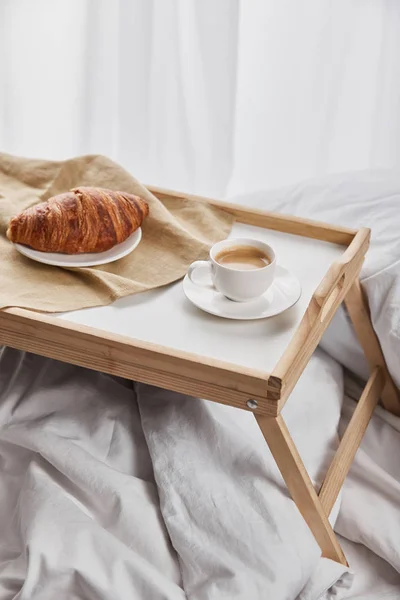 Свежий круассан с кофе на деревянном подносе в постели по утрам — стоковое фото
