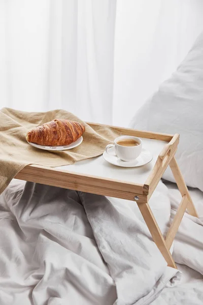 Café e croissant servido em bandeja de madeira na cama branca com travesseiro — Fotografia de Stock