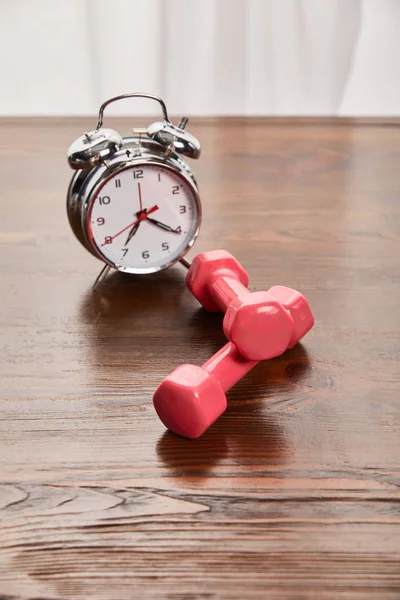 Silver alarm clock near pink dumbbells on wooden table — Stock Photo