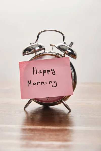 Silberner Wecker mit Happy-Morning-Schriftzug auf rosa Haftnotiz auf Holztisch isoliert auf grau — Stockfoto