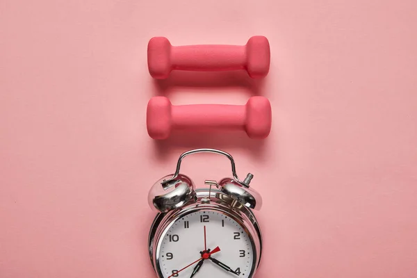 Flat lay with silver alarm clock and pink dumbbells on pink background — Stock Photo