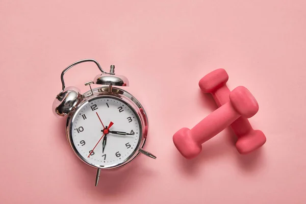 Top view of silver alarm clock and pink dumbbells on pink background — Stock Photo
