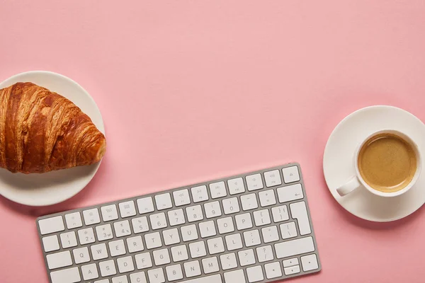 Ansicht der Computertastatur in der Nähe von Kaffee und leckerem Croissant auf rosa Hintergrund — Stockfoto