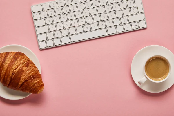 Vista dall'alto della tastiera del computer vicino a caffè e croissant su sfondo rosa — Foto stock