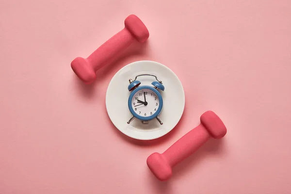 Top view of dumbbells and plate with toy alarm clock on pink background — Stock Photo