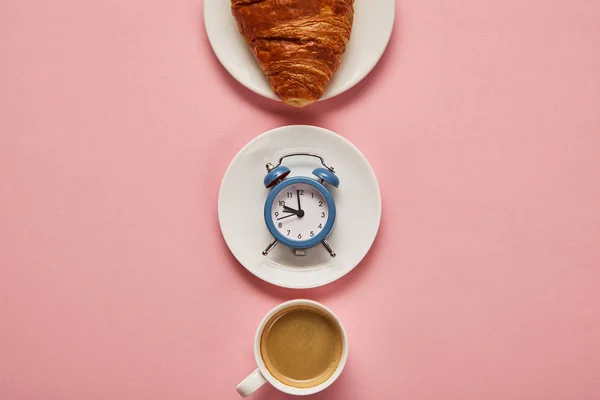 Flat lay com xícara de café, despertador de brinquedo e croissant na placa no fundo rosa — Fotografia de Stock
