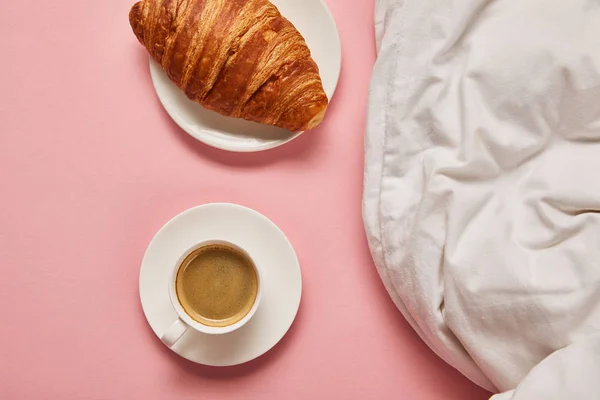Draufsicht auf Decke, Kaffee und Croissant auf rosa Hintergrund — Stockfoto