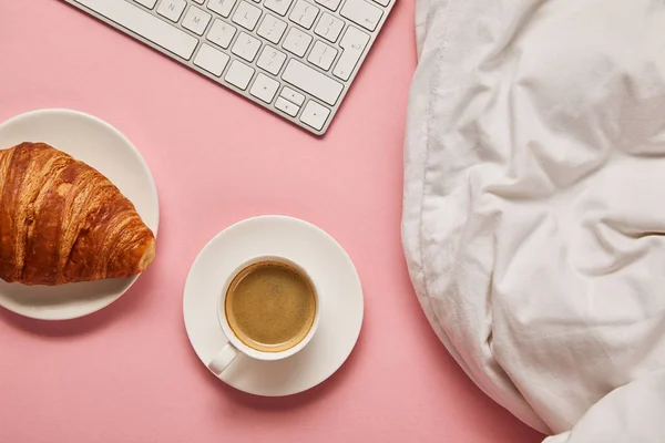 Draufsicht auf Decke, Computertastatur, Kaffee und Croissant auf rosa Hintergrund — Stockfoto