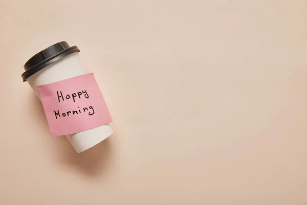 Vista dall'alto del caffè per andare e nota appiccicosa con scritte felici del mattino su sfondo beige — Foto stock