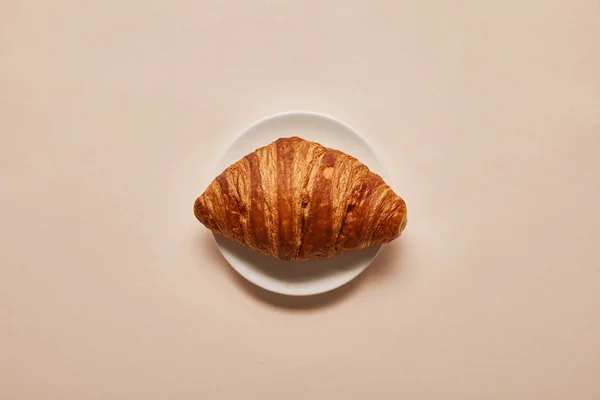 Vue de dessus de croissant savoureux sur plaque blanche sur fond beige — Photo de stock