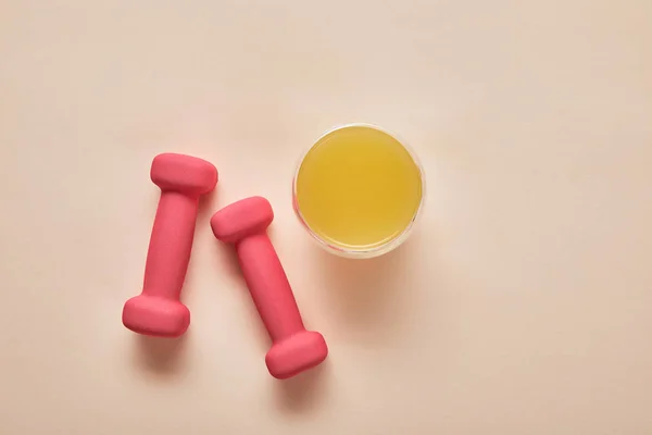 Top view of pink dumbbells, orange juice on beige background — Stock Photo