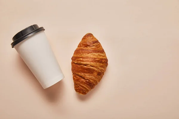 Vista superior del café para llevar y sabroso croissant sobre fondo beige - foto de stock