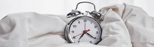Panoramic shot of silver alarm clock covered with blanket in white bed — Stock Photo