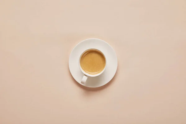 Vista superior del café en taza en platillo sobre fondo beige - foto de stock