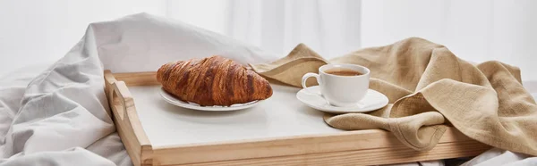 Coffee and croissant served on wooden tray on white bedding, panoramic shot — Stock Photo