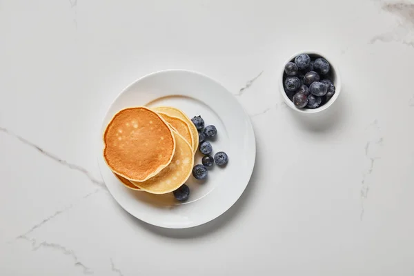 Top view of pancakes in plate near bowl with blueberries on textured surface — Stock Photo