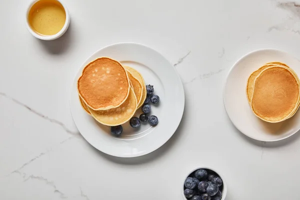 Top view of plates with pancakes and two bowls with honey and blueberries — Stock Photo
