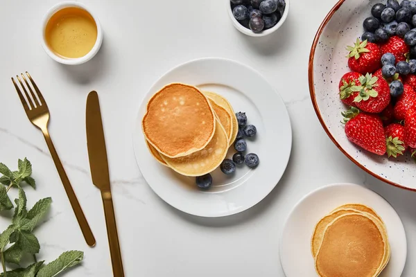 Pfannkuchen, Honig, Blaubeeren, Erdbeeren und Minze in der Nähe von goldenem Besteck — Stockfoto