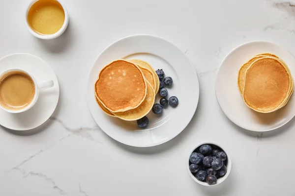 Vista superior de tigelas com mirtilos e mel perto de pratos com panquecas e xícara de café — Fotografia de Stock