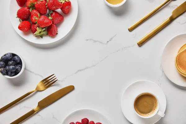 Top view of served breakfast with berries, pancakes and cup of coffee near cutlery and empty space in middle — Stock Photo