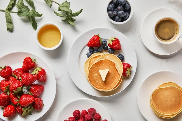 Vista superior del desayuno saludable con fresas, arándanos, frambuesas, tortitas, miel y taza de café - foto de stock