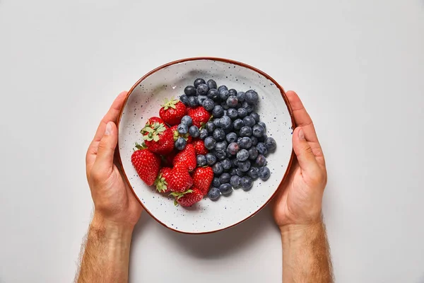 Vue recadrée de l'homme tenant grande assiette avec de savoureuses fraises et des baies bleues — Photo de stock
