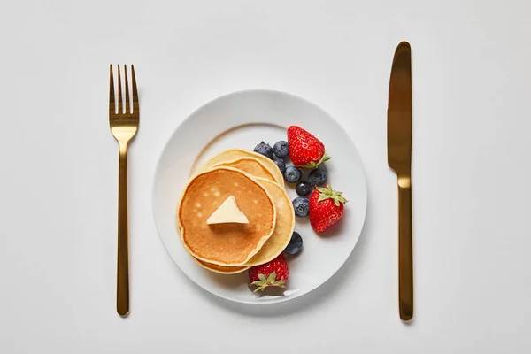 Erdbeeren, Blaubeeren und Pfannkuchen auf Teller in der Nähe von goldener Gabel und Messer — Stockfoto