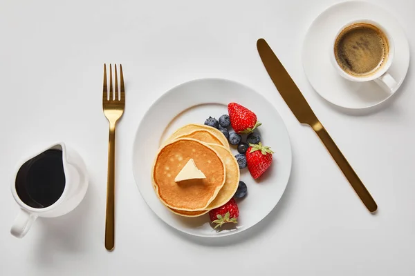 Vue de dessus des crêpes, sirop dans la cruche et tasse de café près de couverts dorés — Photo de stock