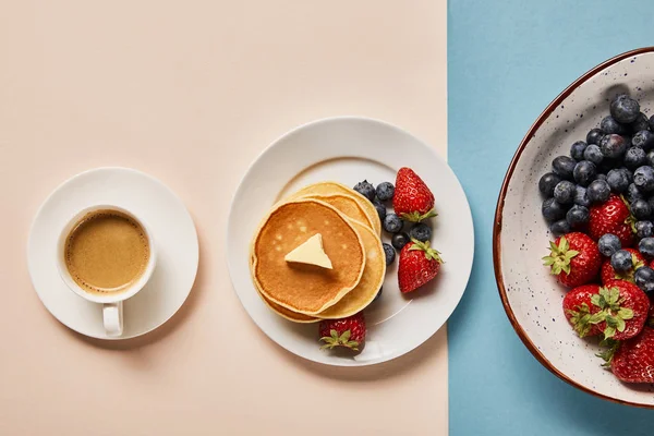 Top view of pancakes with berries on plate near cup of coffee and plate with strawberries and blueberries — Stock Photo