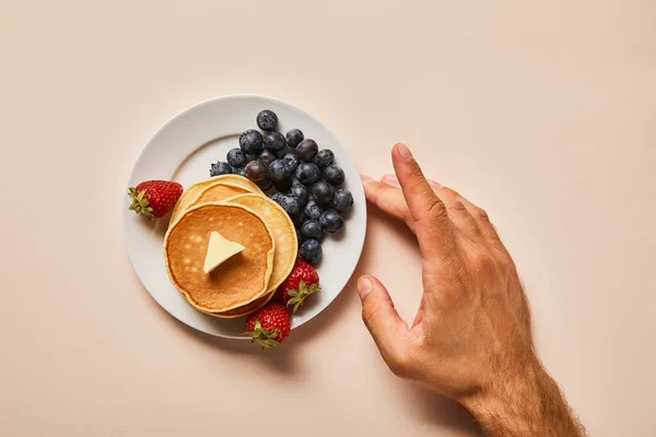 Cropped view of man touching plate with pancakes and berries on pink — Stock Photo